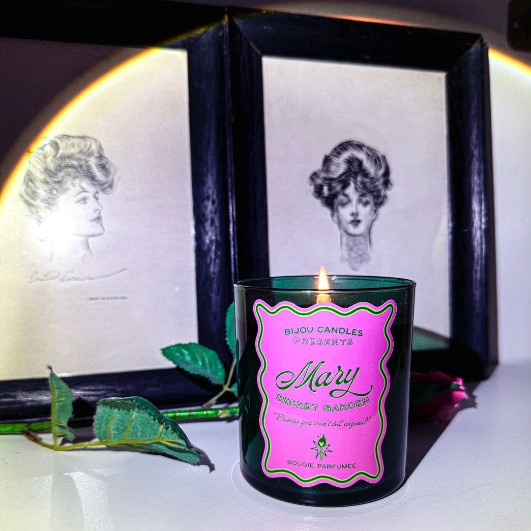 Candle with a pink label in front of a black frame with vintage-style portraits.