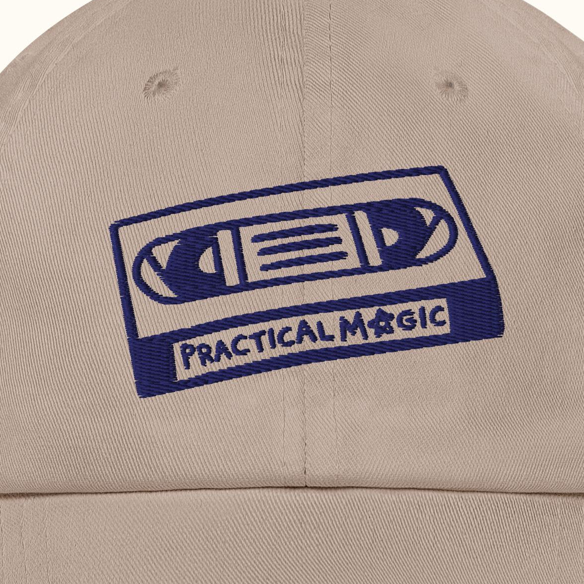 Beige cap with blue cassette tape design and 'Practical Magic' text on a white background