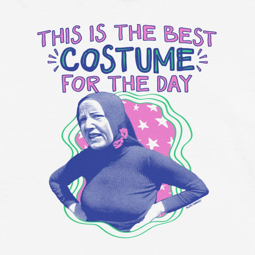 A white short-sleeve graphic t-shirt featuring a printed design of a woman in a black bodysuit with the text 'THIS IS THE BEST COSTUME FOR THE DAY' in purple and blue lettering.
